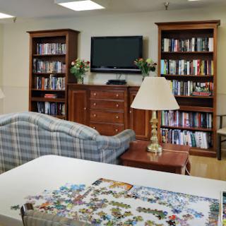 A cozy living room featuring a sofa, bookshelves filled with books, a television, and a table with a jigsaw puzzle.