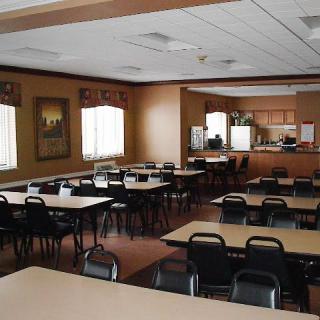 An empty dining room with multiple tables and chairs, resembling a community hall setting.