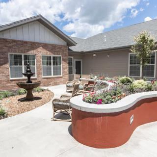 A peaceful courtyard with a fountain, surrounded by seating and a garden in front of a brick building.