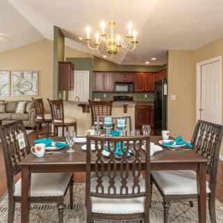 A stylish dining area with a set table, adjacent to a modern kitchen, illuminated by an elegant chandelier.