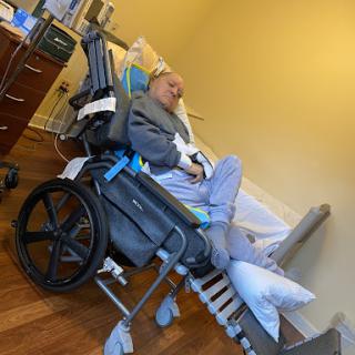 A patient resting in a specialized wheelchair within a hospital room.