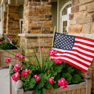 An American flag displayed in a flower planter with vibrant pink blooms.