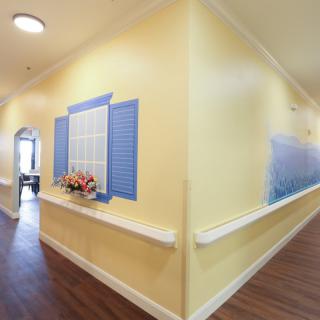 A hallway with yellow walls and blue decorative shutters, featuring a wooden floor and handrails.