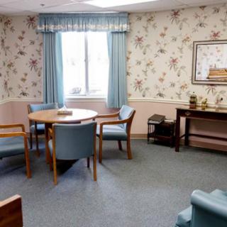 A cozy living room with floral wallpaper, featuring a round table, chairs, and blue curtains.