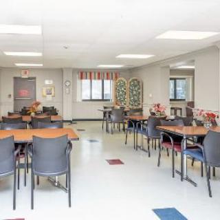A bright community room with tables and chairs arranged neatly, featuring decorative elements and colorful floor tiles.