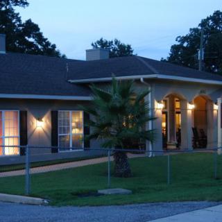 A well-lit house exterior during the evening with surrounding landscaping.