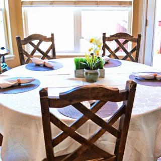 A neatly set dining table with wooden chairs and a floral centerpiece in a well-lit room.