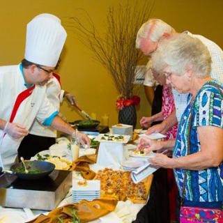 A chef is serving food to guests at a buffet event.
