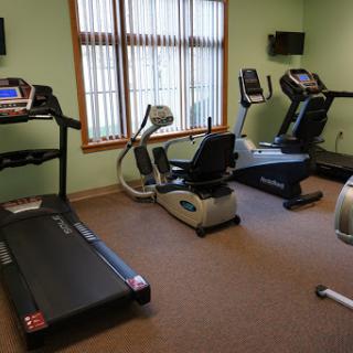 A well-equipped indoor gym featuring a treadmill, elliptical machine, and exercise bike under natural light.