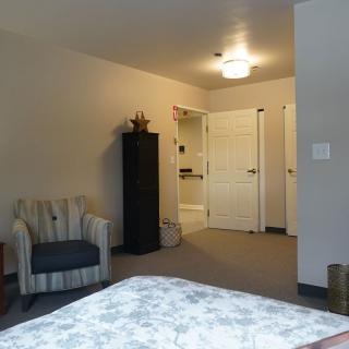 A cozy bedroom featuring a striped chair, tall cabinet, and visible doorway.