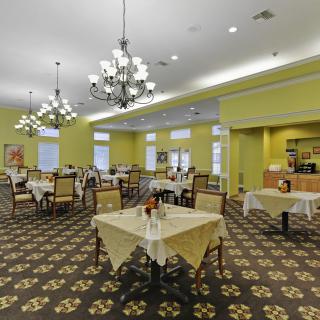 An elegant dining room with yellow walls and chandeliers, featuring several tables and chairs arranged neatly.
