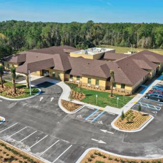 Aerial view of a building with surrounding parking lots and landscaped areas on a sunny day.