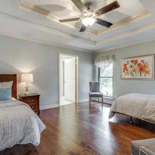 A spacious bedroom with two beds, wooden flooring, a ceiling fan, and a nightstand with a lamp beside the bed.