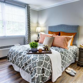 A stylishly decorated bedroom featuring a comfortable bed with gray and orange accents, enhanced by natural light from a nearby window.