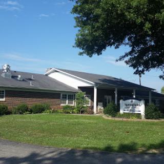 A healthcare clinic surrounded by green grass and trees under a clear blue sky.