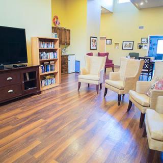 A spacious living room with hardwood flooring, featuring a television, bookshelf, and comfortable chairs.