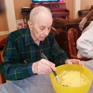 An elderly man enjoys preparing a meal in a cozy home setting.