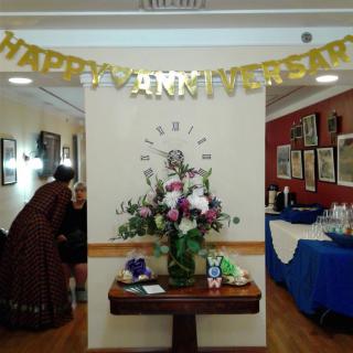 A festive setting for an anniversary party featuring a 'Happy Anniversary' banner and a floral arrangement on a table.