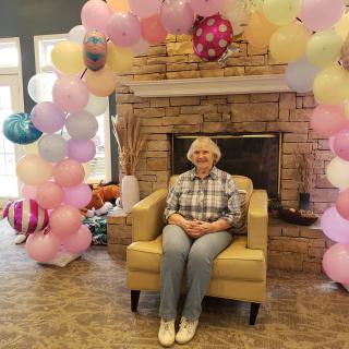 A person sitting on a chair surrounded by festive balloons in front of a fireplace.