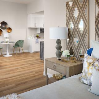 A modern interior featuring a cozy bedroom with stylish decor, a lamp on the nightstand, and a small dining area with contemporary chairs in front of a wooden floor.