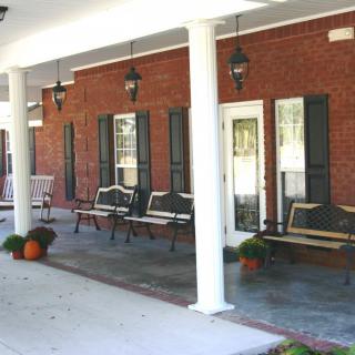A cozy porch with chairs and autumn decorations, featuring columns and lantern-style lights.