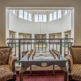 A well-lit interior space featuring a chess table and two comfortable chairs, surrounded by large windows.