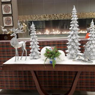 A festive holiday display featuring silver Christmas trees and a decorative reindeer, set against a cozy fireplace.