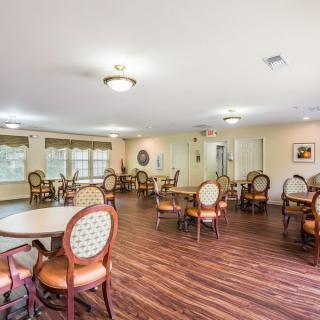 A well-lit dining area with several tables and chairs, featuring hardwood floors and large windows.