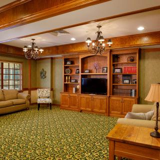 A cozy living room with wooden shelves and a television, featuring comfortable sofas and warm lighting.