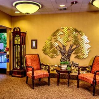 A warmly decorated lobby with two chairs, a table, a grandfather clock, and metal tree wall art.