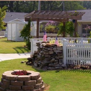 A cozy outdoor garden area featuring a fire pit, pergola, and white fence.