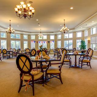 A spacious dining room with elegant chandeliers, surrounded by large windows and furnished with round tables and chairs.