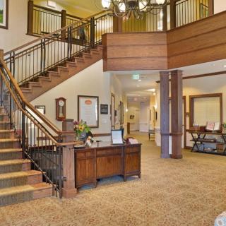 A spacious lobby area featuring a grand staircase with wooden railings, a reception desk, and elegant lighting.