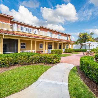 A residential building with a landscaped garden and pathway under a partly cloudy sky.