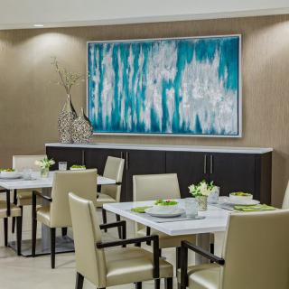 A modern dining room with elegant decor, featuring a large abstract painting and neatly arranged tables and chairs.