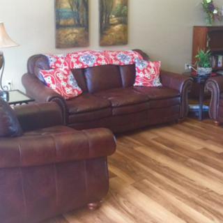 A cozy living room featuring a leather sofa with decorative pillows, wooden flooring, and artwork on the wall.