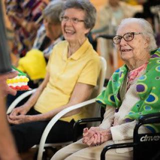 Two elderly women smiling and enjoying a community gathering indoors.