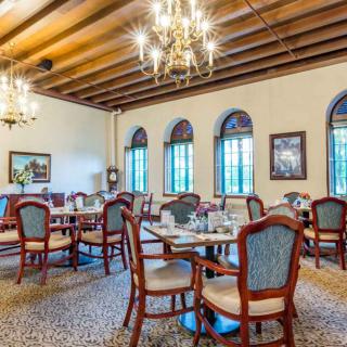 An elegant dining room with multiple tables and chairs, featuring large windows and chandeliers.