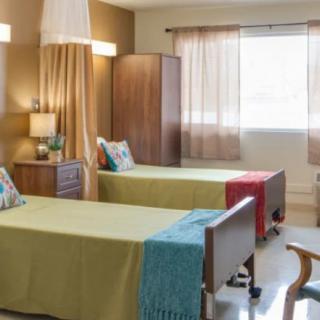 A well-lit hospital room with twin beds, colorful pillows, and cozy decor.