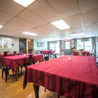A cozy restaurant dining area featuring tables with red tablecloths and ample natural light.