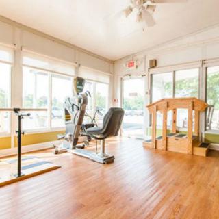 A bright and spacious gym with exercise equipment and wooden flooring.
