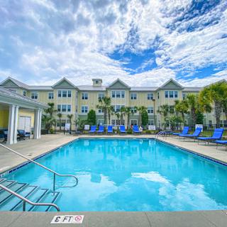 A serene outdoor swimming pool surrounded by a modern apartment complex under a beautiful blue sky.