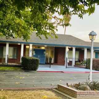 A small building with a blue door and white pillars, surrounded by trees and a parking area.
