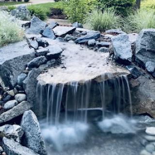 A serene waterfall cascading over smooth stones, surrounded by lush greenery.
