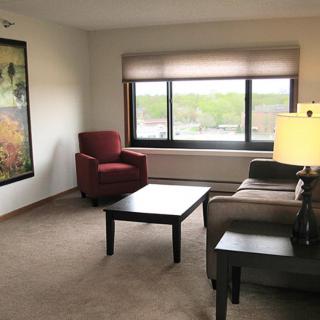A cozy living room with a sofa, armchair, coffee table, and a large window providing natural light.