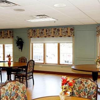 A bright dining area with tables, chairs, and floral-patterned decor near large windows.