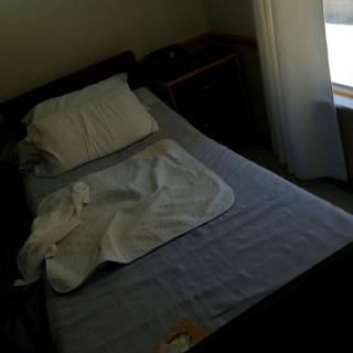 A messy bed in a dimly lit bedroom with a window nearby.