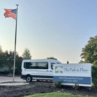 A van parked near a building sign with an American flag flying nearby.