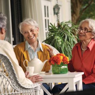 Three seniors enjoying a relaxed conversation over tea on a porch.