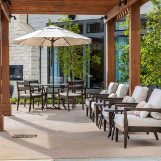 A modern patio setup featuring cushioned chairs, a pergola, and an outdoor dining table with an umbrella.